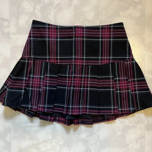 Rutig miniskirt - Svart-och rosarutig minikjol. Från Divided. Storlek 34.  Eftersom jag inte får på mig den visar jag bara upp den framför mig :)