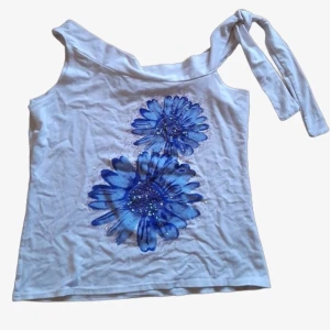 Unik topp med blomtryck - Vit knyttopp (knyts på ena axeln) glittrigt tryck, blåa blommor passar s-l beroende på önskad passform