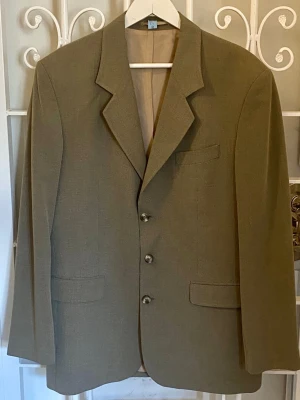 Retrokavaj 90-tal – Joyboy - Smårutigt textilmönster, grågrönbeige färg. Fint skick.  Storlek: 150 45 % viskos. 55 % polyester. Foder: 100 % acetat.