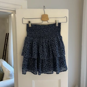Volangkjol med leopardmönster  - En söt volangkjol med blå grund och svart leopardmönster. Endast använd 1 gång så superskick. Storlek 146/152 men skulle säga att den motsvarar en xs.
