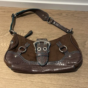 Guess väska  - Fin väska i brunt tyg med blå detaljer, passar till allt! Längd på väskan ca 33 cm!