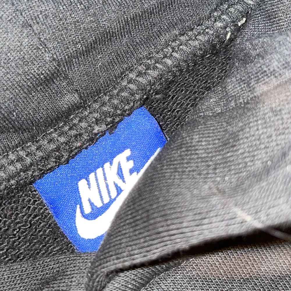 Den är svart med vit märke där det står ”Nike”. Stickat.