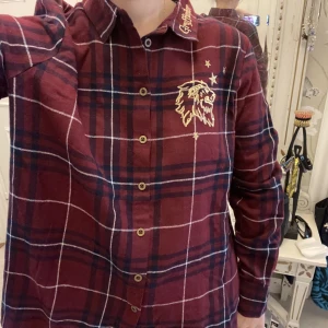 Harry potter shorta med Gryffindor tryck på.  - Snygg Harry Potter shorta med fint broderi med ett Lejon, med broderad guld text med texten Gryffindor på kragen. Om ni undrar något så tveka inte att höra av er. 🤍❤️