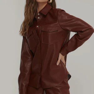 PU-skjorta från Na-kd  - En super snygg brun PU-skjorta med dubbla fickor från Na-kd. Storlek 38. Väldigt fint skick, använt endast fåtal gånger.