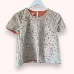 Matthew Williamson kort beige/persikofärgad blus strl S-Xs - Kort blus i två lager från Matthew Williamson. Undre lagret är enfärgat i typ persika, det övre lagret är grå/beige spets i form av blommor. Bra skick allmänt sett, dock slitage på tråden till knappen, se sista bilden. Storlek S, något liten i storleken.