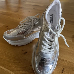 Silvriga sneakers med platå - Silvriga sneakers från Nelly. Jättesnygga och sköna, men säljer då de aldrig kommer till använding :) Dem är bara använda ett fåtal gånger för några år sedan, kan ha några enstana fläckar