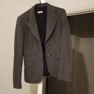 Fin kavaj  - Den är fin, grå och proffsigt, en av knapperna är lite söder men den ser fint ändå. 