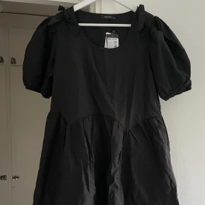 Svart klänning - Svart klänning med söta rosetter i storlek 40. Helt oanvänd.