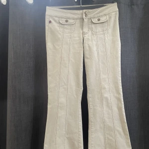 Beiga lågmidjade byxor  - As snygga beiga byxor med coola detaljer, utsvängda och lågmidjade😍😍Aldrig använda. Midjemått 38cm, innebensläng 71cm☺️