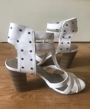 Vita klackskor med nitar - Säljer ett par vita klackskor med detaljer av nitar. Klackskorna är endas använda 2 gånger och är i nyskick. Storlek 39