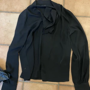 Svart blus - Tunt material, nästan mesh men inte genomskinligt. Rosett vid halsen. Tror att den är köpt på hm eller zara