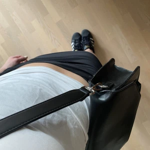 Svart axelremsväska - Svart axelremsväska med justerbart band, rymlig med flera fack på insidan. Finns vissa tecekn på användning men genrellt bra skick