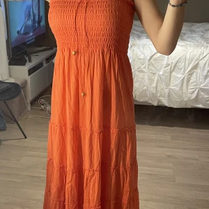 Lång sommarklänning  - Aldrig använt. Går att knyta fram och spänna så den håller upp sig. Väldigt lång den når nästan ner i marken på mig. Köpt på Gina Tricot och är storlek 38. Fin corallaktig färg.