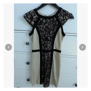 Cocktail klänning 34 - Kort, figursydd klänning i beige med svarta lace detaljer. Dragkedja i ryggen. Storlek 34.  Köpt från Missguided, aldrig använd, prislapp kvar och inga skavanker.