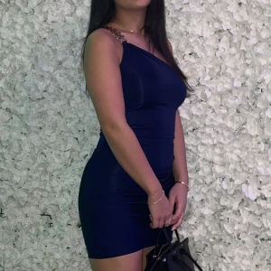 Mörkblå festklänning  - Mörkblå festklänning med en arm med guldig detalj, endast använd en gång, Storlek S