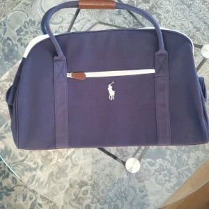 RALPH LAUREN WEEKEND-VÄSKA. OANVÄND. - Ralph Lauren weekend-väska. Helt oanvänd. Perfekt för helgresan. Kan bäras i handen eller över axeln.