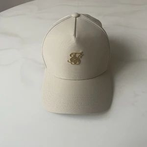 Keps från Silksilk - Beige keps med guldlogga, aldrig använd så kepsen är i nyskick. Justerbar.