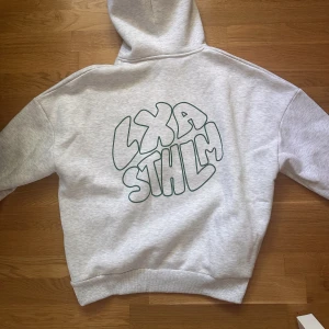 LXA hoodie - Ljusgrå med grönt tryck på ryggen. Knappt använd, mycket gott skick. Storlek medium. 