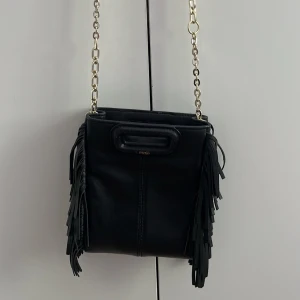 Maje Väska Liten - Säljer denna Maje väska, i storleken Mini. Kommer med ett långt band som man ser på 3:dje bilden, även en kort guld-kedja. Pris kan diskuteras. Köpt på NK för 2 400kr!🩷