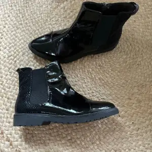 Svarta ankelboots från TAMARIS storlek 37. Lack framtill och ormskinnsimitation bak. Helt nya och endast provade inomhus. Nypris runt 900kr, mitt pris: 300kr.