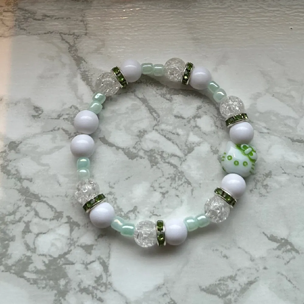 Handgjort armband med gröna detaljer & hello kitty pärla! 🤍 ca 16 cm runt. Gjord med dubbla snören för säkerhet 🩵 Köp genom köp nu! Eller privat via swish (frakt 15 kronor). Accessoarer.