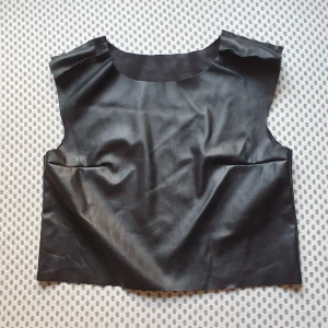 Svart top i fejkläder - Svart top i tunt fejkläder. Står ingen storlek men gissar S, kanske M. Nyskick. Snygga detaljer på axlarna (bild 2).