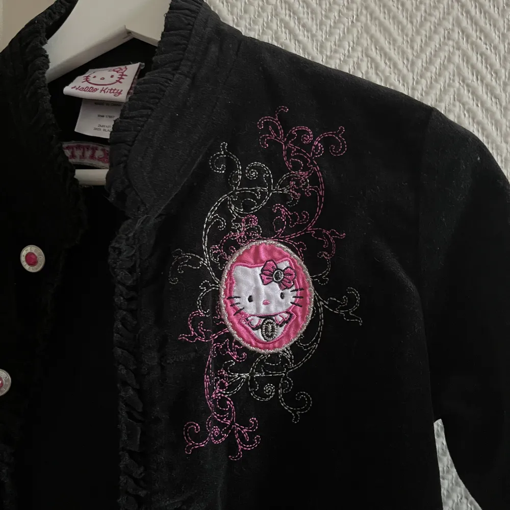 Hello Kitty tröja/kavaj/jacka i ett sammetsliknande tyg med Kitty-”emblem/broderi och knappar med rosa stenar💕  (Made in China, står storlek L men är mer som en XS) Längd 47cm. Bredd vid axlar 37 cm. Bredd under ärmarna 40 cm.  . Tröjor & Koftor.