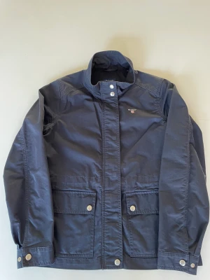 GANT vårjacka till barn - Marinblå vårjacka från GANT, storlek 146/152, 11-12 år säljes. Jackan är sparsamt använd och i mycket fint skick.