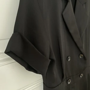 Supersnygg jumpsuit - Svart och fin jumpsuit med snygga detaljer. Sitter tight över höften med är lite oversize upptill (som en skjorta) och har vita ben. Lyxigt material.
