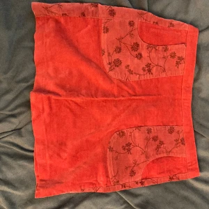 Kjol i mocca-liknande tyg - Supersöt kjol med fickor, blommiga detaljer och tyg som liknar mocca. Röd/brun färg.  