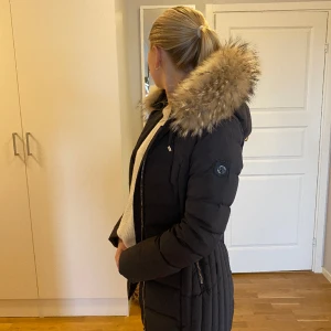 Vinterjacka med pälsluva - Vinterjacka från Hollies. Knappt använd. Varm och lätt att ta av pälsen på luvan. Brun/grå färg. Strl 34 men passar upp till strl 38