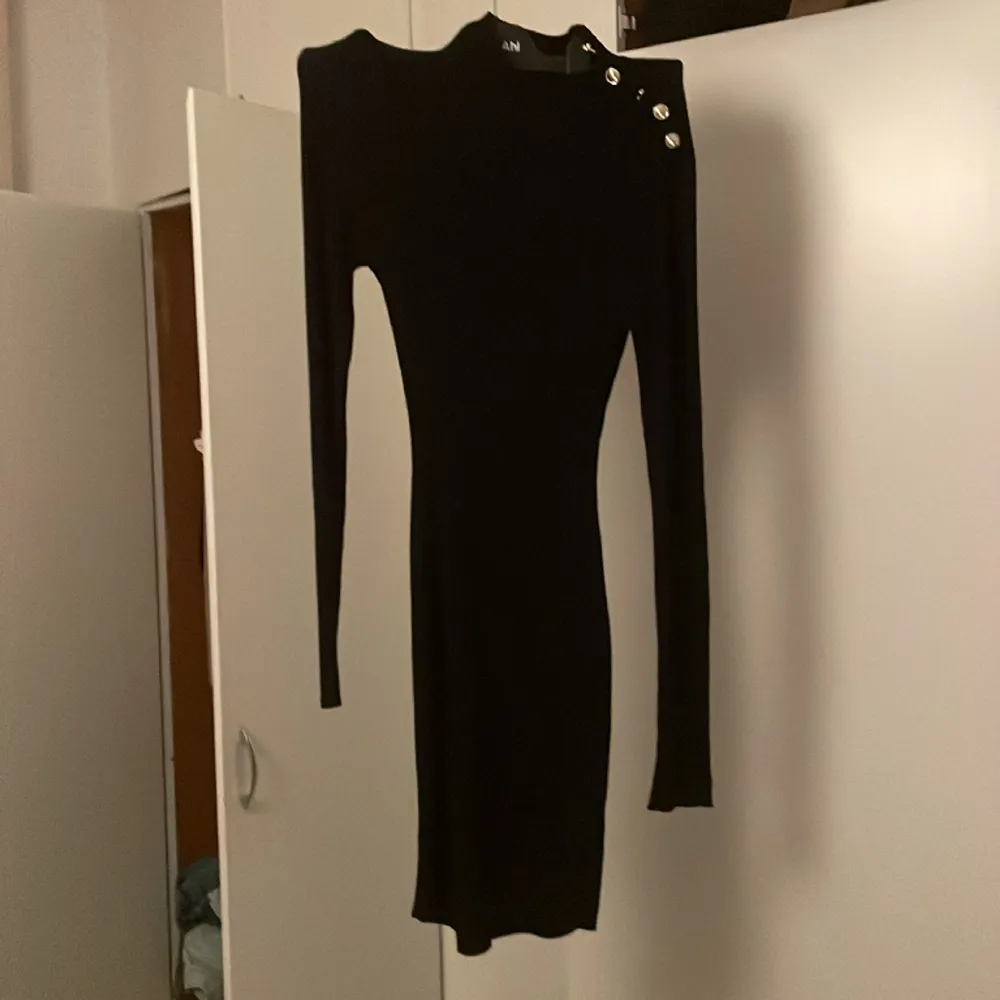 En vanlig svart klänning förutom att den har snygga guldiga knappar på sidan. Klänningar.