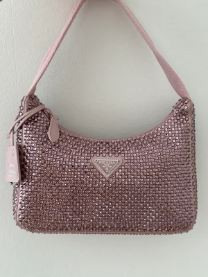 Re-Edition 2000 glitter handbag  - This mini hobo bag, an iconic Prada style, comes in a luxurious satin version studded with crystals and decorated with the emblematic enamel triangle logo.