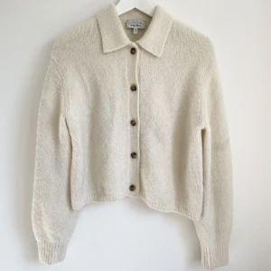 Stickad tröja med knappar  - Mjuk och skön stickad tröja med knappar och krage i benvit färg. Skick: använt  Material: 40% alpacka 25% ull 35% polyamid  Nypris: ca 700kr 