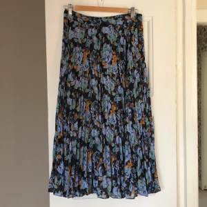 Plisserad kjol - Blommig veckad kjol i 100% Polyester - halvfodrad på insidan med ett viskosfoder. Dold dragkedja i sidan. Ca 80 cm lång. 
