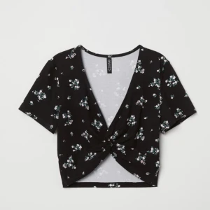 DIVIDED blommig topp (M) - Kort topp i mjuk viskosjersey med tryckt mönster. V-ringad, korta ärmar och något kortare framparti med knytdetaljer nedtill💐