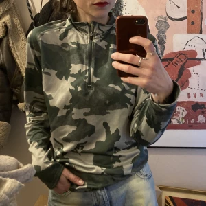 90s kamouflagetröja - Tunn sportaktig tröja med krage med dragkedja. Snyggt att ha till baggy jeans tex! Mycket bra skick. 