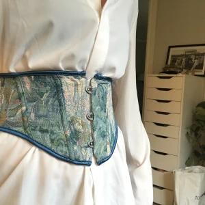 Blå/grön  korsett - En jättefin blå/grön korsett med mönster på. Bara använts en gång till skolavslutningen. Jätte fint skick. Säljer den för att den bara inte används längre!😊