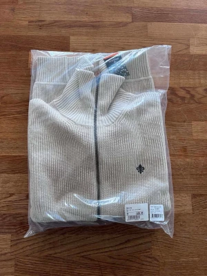 NY beige cardigan från Morris - Helt ny beige cardigan från Morris, aldrig använd. Stickad modell med hög krage och dragkedja framtill. Klassisk och stilren färg som passar till det mesta.  Nypris: 1 899 kr. Säljes för 999 kr.  Skickas i originalförpackning.