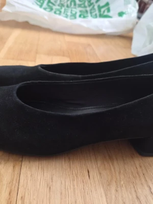 Svarta Vagabond klackskor i mocka storlek 41 - Säljer ett par jättefina och eleganta svarta klackskor från det populära märket Vagabond Shoemakers i storlek 41. Skorna är tillverkade i äkta, mjuk mocka och har en klassisk, tidlös design med spetsig tå som passar perfekt till både fest, kontor och finare tillfällen. De är sparsamt använda och i ett mycket välvårdat skick med fina sulor, och de erbjuder den stabila komfort och höga kvalitet som Vagabond är kända för.  Finns för avhämtning i Malmö.