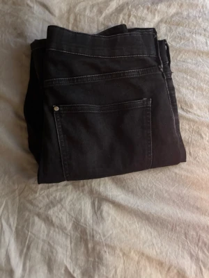 Svarta raka jeans - Säljer ett par svarta jeans med rak passform och klassiska fem fickor. Jeansen har silverfärgad knapp och kontrastsömmar. Materialet är denim i bomull. Perfekta för en stilren och enkel look. (Strlk 170)