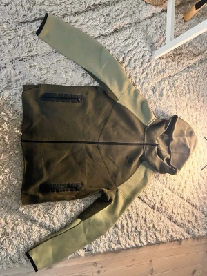 Olivgrön hoodie från Nike XL - Säljer en olivgrön hoodie från Nike i storlek XL. Hoodien har hel dragkedja framtill, två svarta dragkedjeförsedda fickor och en skön huva. Materialet känns mjukt och sportigt, perfekt för chill eller träning. Snygg kontrast mellan ärmar och kropp.