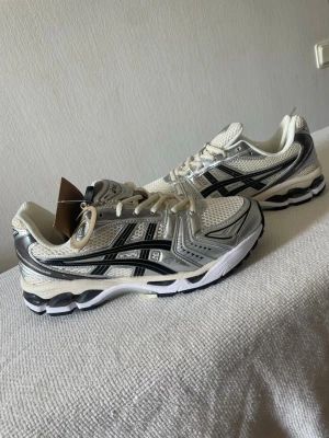 Silvriga och vita sneakers med mesh - Snygga sneakers i silver och vitt med svarta detaljer. Ovandelen är i mesh och syntetmaterial för en sportig look. Skorna har en chunky sula i vitt och svart samt klassisk snörning. Perfekta för dig som gillar retrostil och streetwear.