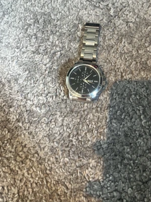 Stilren silverfärgad klocka med länk - Snygg klocka med svart urtavla och flera små visare. Armbandet är i blankt silverfärgat metall och har en klassisk länkdesign. Urtavlan har tydliga markeringar och en modern look som passar till många stilar.