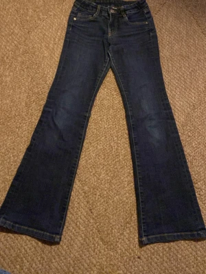 Mörkblå bootcut jeans - Snygga mörkblå bootcut jeans med klassisk femficksdesign och utsvängda ben. Jeansen har normalhög midja och detaljerade bakfickor med lock och knapp. Perfekta för en trendig och avslappnad look.