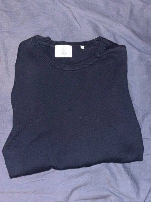 Svart stickad tröja från Bläck - En stilren svart stickad tröja från Bläck med rund halsringning och ribbade muddar. Perfekt att matcha med jeans eller kjol för en clean look. Materialet känns mjukt och bekvämt mot huden.