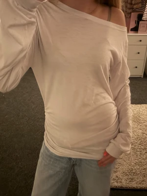 offshoulder långärmad topp - Säljer en vit långärmad topp med offshoulder-design och lätt rynkade sidor. Toppen har en avslappnad passform och är gjord i mjukt bomullsmaterial. Perfekt att styla med jeans för en chill look. Tröjan har scrunh vid sidan 🥰
