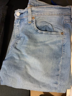 Ljusblå raka Levis jeans med hög midja - Säljer ett par ljusblå jeans med rak passform och hög midja. Klassisk femficksmodell med knapp och dragkedja framtill. Jeansen är i ett mjukt denimtyg och har subtila slitningar för en avslappnad look.