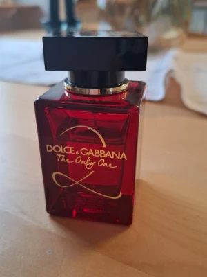 Dolce & Gabbana The Only One parfym - Snygg parfymflaska i djupt rött glas med svart fyrkantigt lock från Dolce & Gabbana. Flaskan har guldfärgad text och elegant design, perfekt för dig som vill ha en exklusiv doft på hyllan. More than 40ml remaining. No box available. Bought few months ago. 
