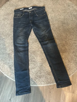   jeans SACRE DENIM - Snygga mörkblå  jeans från SACHE DENIM med klassisk femficksdesign och diskret logga på myntfickan. Jeansen har slitningar och tvättade detaljer för en trendig look. Perfekta för dig som gillar en smal passform och stilren design.